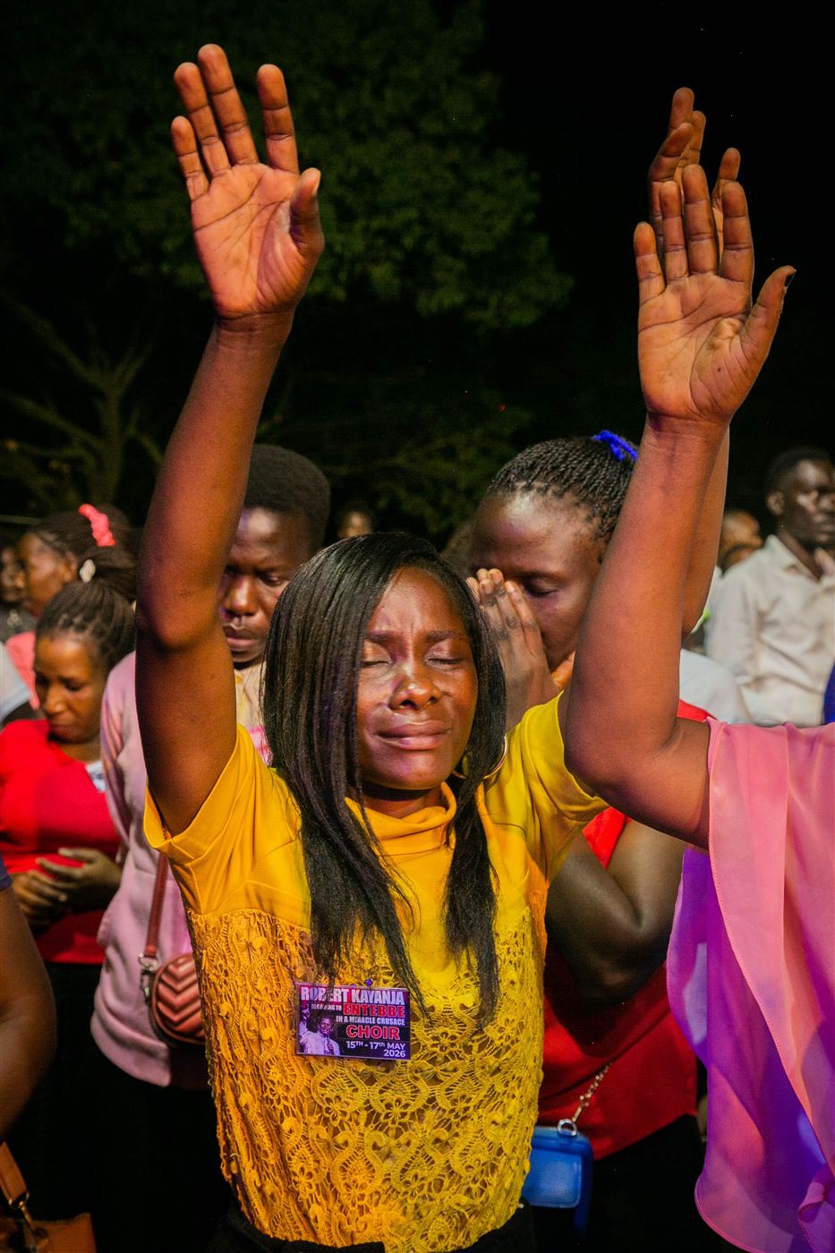 A woman worshipping with both arms raised, eyes closed in tears