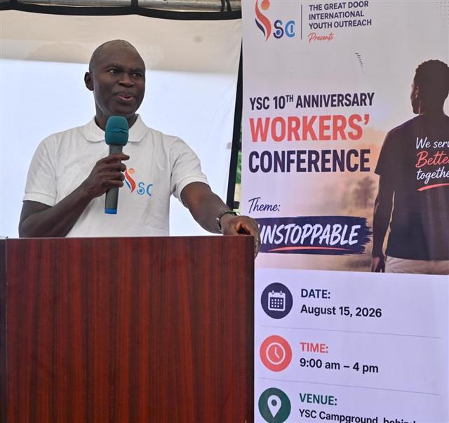 Pastor Olayiwola speaking at a podium beside a Workers' Conference banner