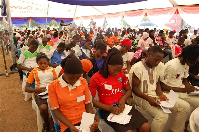 Students seated under a large tent listening to a speaker